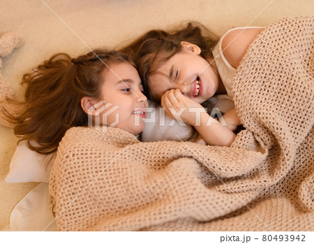 girls is lying on the floor and talking or sleeping, and cover themselves with a blanket, home interior decorated with holiday lights and gifts girls is lying on the floor and talking or sleeping, and cover themselves with a blanket, home interior decorated with holiday lights and gifts 80493942