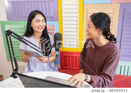 an asian girl using a tablet while chatting with her friend using a laptop in front of a microphone 80493952
