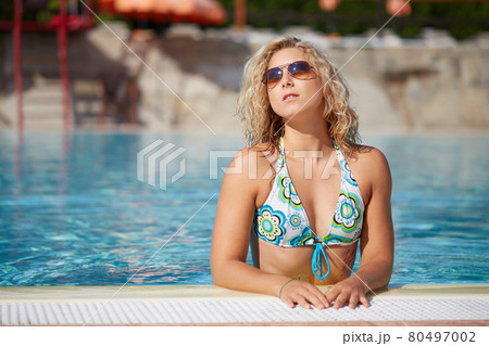 curly blond girl relax at swimming pool 80497002
