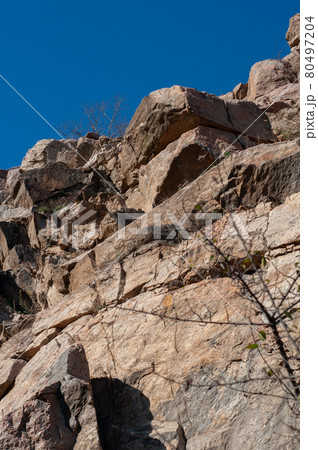 Granite rocks close-up on background blue sky with white clouds, green leaves on treetops. Granite rocks close-up on background blue sky with white clouds, green leaves on treetops. 80497204