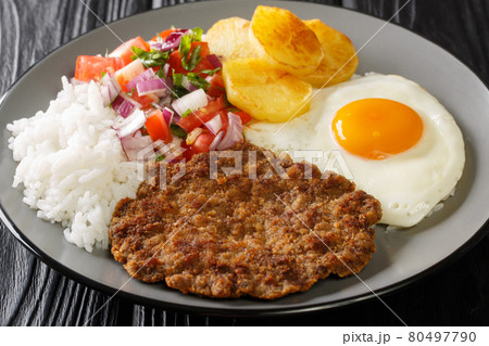 Silpancho Rice golden potatoes, beef, and fried eggs are topped with an onion and tomato salsa in this traditional Bolivian dish closeup in the plate. Horizontal 80497790