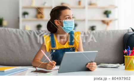 Schoolgirl in medical mask studying remotely with digital tablet 80497902