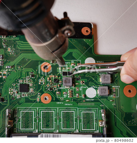 Repairman is using tweezers and hot air blower to fix motherboard. Repairman is using tweezers and hot air blower to fix motherboard. 80498602