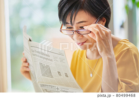 老眼鏡を掛けて英字新聞を読むミドル女性 80499468