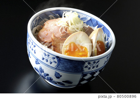 キャベツの千切りに味玉、ネギがトッピングされた湯気が立つ焼豚丼を黒背景で撮影 80500896