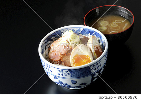 キャベツの千切りに味玉、ネギがトッピングされた湯気が立っている焼豚丼と味噌汁のセットを黒背景で撮影 キャベツの千切りに味玉、ネギがトッピングされた湯気が立っている焼豚丼と味噌汁のセットを黒背景で撮影 80500970