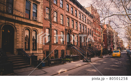 Row of old brownstone buildings along an empty sidewalk block in the Greenwich Village neighborhood of Manhattan, New York City NYC Row of old brownstone buildings along an empty sidewalk block in the Greenwich Village neighborhood of Manhattan, New York City NYC 80501258