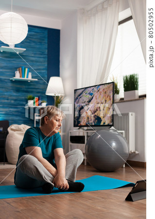 Retired senior woman in sportswear sitting on yoga mat watching fitness lesson on laptop Retired senior woman in sportswear sitting on yoga mat watching fitness lesson on laptop 80502955