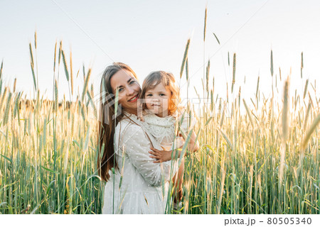 Happy family, mother in a dress with a cute little baby on a golden wheat field at sunset. summer day 80505340