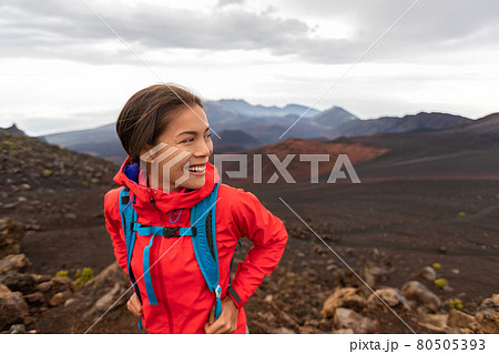 Hiking Asian woman in outdoor volcano landscape walking in Hawaii. Happy hiker on trek with backpack and red rain jacket. Hiking Asian woman in outdoor volcano landscape walking in Hawaii. Happy hiker on trek with backpack and red rain jacket. 80505393