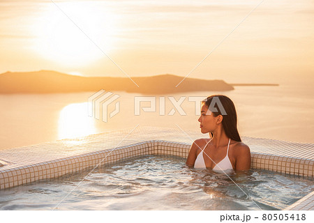 Luxury resort woman swimming in jacuzzi hot tub outside on private hotel room balcony watching sunset over Mediterranean sea. Europe honeymoon vacation. 80505418