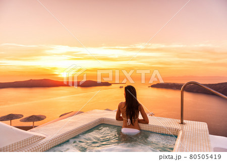 Luxury travel Santorini vacation woman swimming in hotel jacuzzi pool watching sunset. Europe resort destination holiday for honeymoon getaway. 80505419