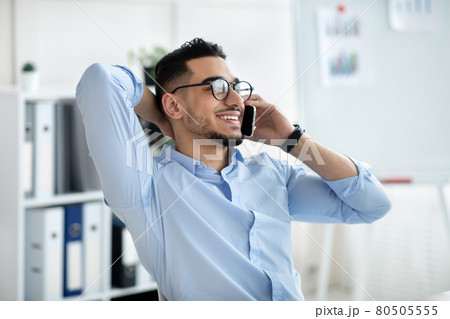 Handsome young Arab man in office wear talking on mobile phone at workplace 80505555