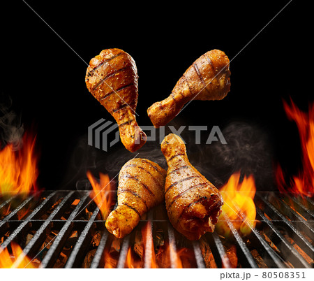 Falling down barbecue bbq grilled chicken drumsticks with golden crust and spices. Flaming fire, ember charcoal, smoke on black background. Close up 80508351