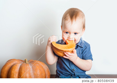 Baby in denim overalls and pumpkin. Toddler and concept of pumpkin puree, harvest, food allergies, healthy eating and first feeding. Baby in denim overalls and pumpkin. Toddler and concept of pumpkin puree, harvest, food allergies, healthy eating and first feeding. 80508439