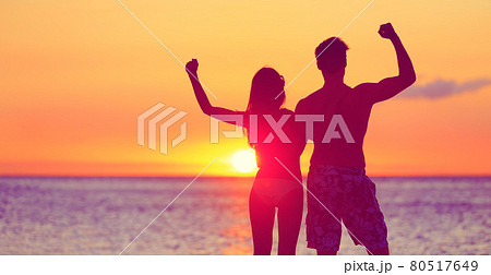 Happy fitness people on beach at sunset flexing 80517649