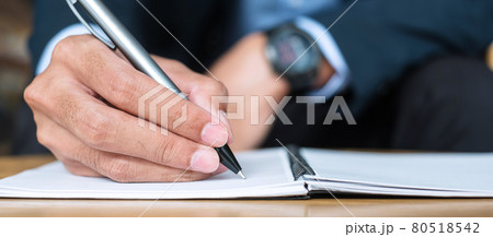 Businessman in suit writing something on notebook in office or cafe, hand of man holding pen with signature on paper report. business concepts Businessman in suit writing something on notebook in office or cafe, hand of man holding pen with signature on paper report. business concepts 80518542