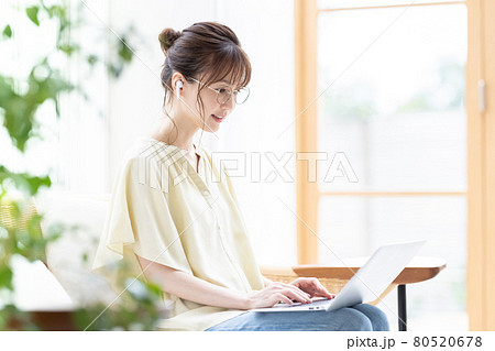 イヤホンを付けてパソコンを見る若い女性 80520678