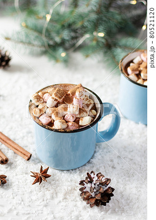 Spicy hot chocolate with cinnamon, star anise and marshmallows in enamel blue mug on white background with Christmas decorations. Spicy hot chocolate with cinnamon, star anise and marshmallows in enamel blue mug on white background with Christmas decorations. 80521120