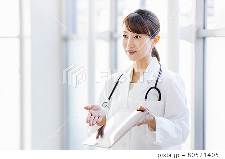 フレーム外の人物にタブレット端末の画面を見せる女性医師 80521405
