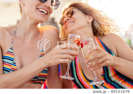 Two young adult girlfriends enjoy have fun celebrate happy moments drinking and cheers champagne wine glasses at ocean sea beach summer vacation. LGBT bisexual lifestyle life and travel concept 80531076
