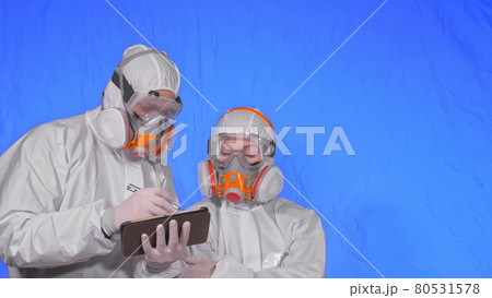 Scientist virologist in respirator makes write in an tablet computer with stylus. Man and woman wearing protective medical mask. Chroma key blue. 80531578