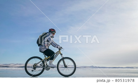 Woman is riding bicycle on the ice. Tires on bike are covered wi 80531978