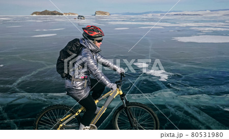 Woman is riding bicycle on the ice. Tires on bike are covered wi 80531980