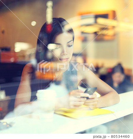 Cafe city lifestyle woman on phone drinking coffee texting text message on smartphone app sitting indoor in trendy urban cafe. Cool young modern mixed race Asian Caucasian female model in her 20s. 80534460