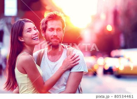 Happy Asian woman, Caucasian man multiethnic couple relaxing in sunset laughing smiling on urban city street in New York city, USA. Young people in love living a modern lifestyle. 80534461