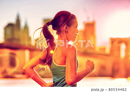 Running woman Asian runner in New York city sunset. Runner jogging in sunny bright light. Female fitness model training outside in New York City with skyline and Brooklyn Bridge in background. 80534462