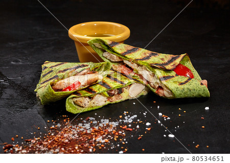 Sliced burrito in spinach tortilla with chicken on black surface Sliced burrito in spinach tortilla with chicken on black surface 80534651