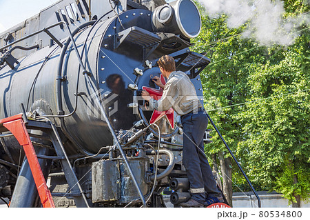 Worker washes a black retro steam locomotive at the railway station 80534800