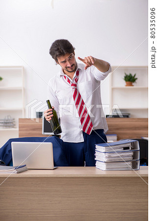 Young alcohol addicted male employee working in the office Young alcohol addicted male employee working in the office 80535096