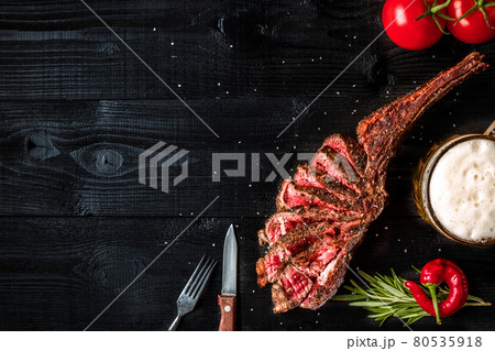 Barbecue dry aged rib of beef with spice, vegetables and a glass of light beer close-up on black wooden background Barbecue dry aged rib of beef with spice, vegetables and a glass of light beer close-up on black wooden background 80535918