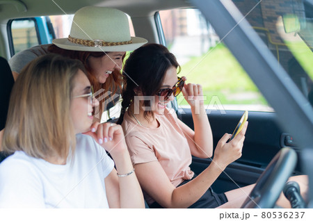 Three happy girlfriends go on a trip. Women are driving in a car and taking a selfie on a mobile phone 80536237
