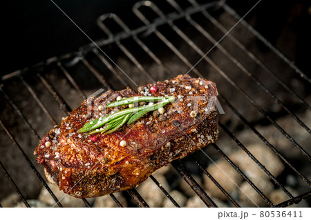 Hot spicy steak grilling on a summer barbecue over the hot coals garnished decorated with a branch of rosemary 80536411