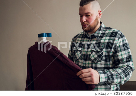 a man puts things in order. holds the garment steamer in his hand and smoothes the jacket after washing. a man puts things in order. holds the garment steamer in his hand and smoothes the jacket after washing. 80537956