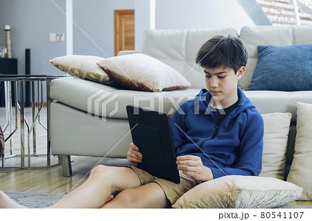The boy using tablet computer while sitting on sofa at home. The boy using tablet computer while sitting on sofa at home. 80541107