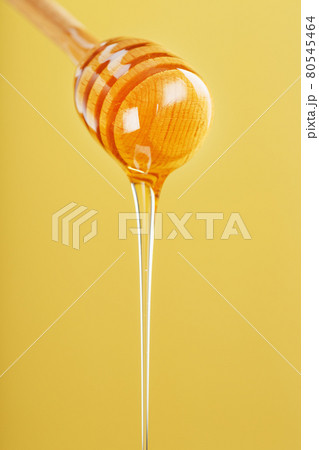 Golden honey trickles from a wooden honey dipper on a yellow background Golden honey trickles from a wooden honey dipper on a yellow background 80545464