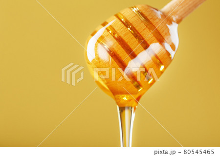 Golden honey trickles from a wooden honey dipper on a yellow background 80545465