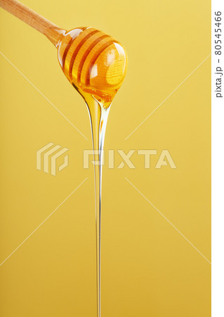 Honey drips in a thin stream from a honey dipper on a yellow background. Honey drips in a thin stream from a honey dipper on a yellow background. 80545466