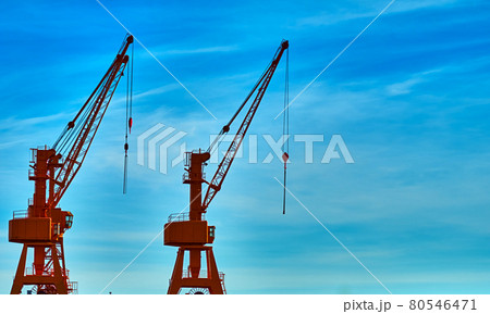 Cargo cranes on the harbor quay against a sky with hazy veil clouds 80546471