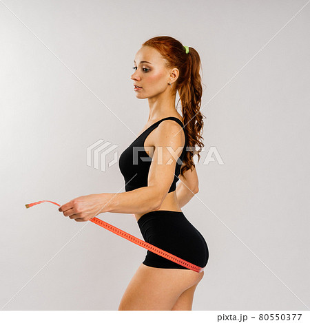 Fitness woman with tape measure showing her waist on studio background Fitness woman with tape measure showing her waist on studio background 80550377