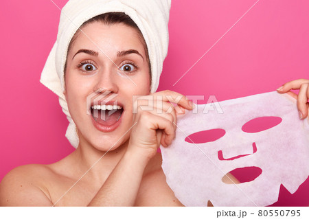 Headshot of amazed beautiful young woman holds cosmetic mask, feels refreshed and energized, has wrapped towel on head, looks with amazement directly at camera, isolated over pink background Headshot of amazed beautiful young woman holds cosmetic mask, feels refreshed and energized, has wrapped towel on head, looks with amazement directly at camera, isolated over pink background 80550795