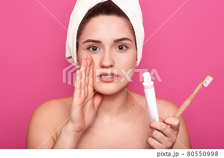 Attractive caucasian woman isolated on pink studio background, young female ready to brush her teeth, being photogrephed with naked shoulders and with white towel on head, keeps hand near mouth. Attractive caucasian woman isolated on pink studio background, young female ready to brush her teeth, being photogrephed with naked shoulders and with white towel on head, keeps hand near mouth. 80550998