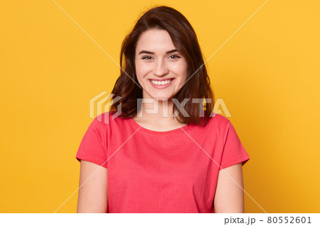 Picture of Caucasian brunette woman posing isolated over yellow background, dark haired lady looks smiling directly at camera, looking happy, lady wearing red t shirt. People emotions concept. Picture of Caucasian brunette woman posing isolated over yellow background, dark haired lady looks smiling directly at camera, looking happy, lady wearing red t shirt. People emotions concept. 80552601