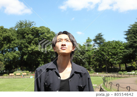 上を見上げる若い男性正面向き青空と緑背景 80554642