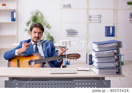 Young male employee playing guitar at workplace Young male employee playing guitar at workplace 80555428