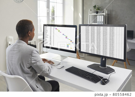 Financial accountant sitting at office desk and working on two desktop computers 80558462